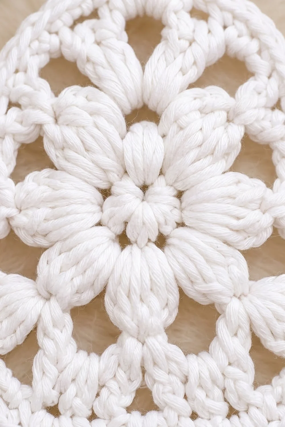 Close-up of white crocheted cotton displaying geometric flower-like motifs with detailed yarn texture against a warm beige background.