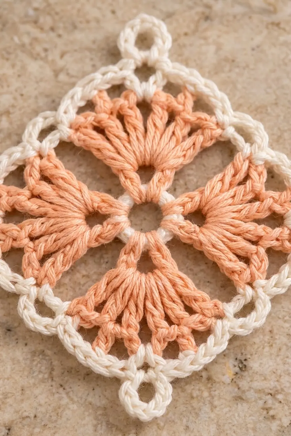 Lacy crocheted ornament in peach and cream yarn with delicate open-work petals on beige linen.
