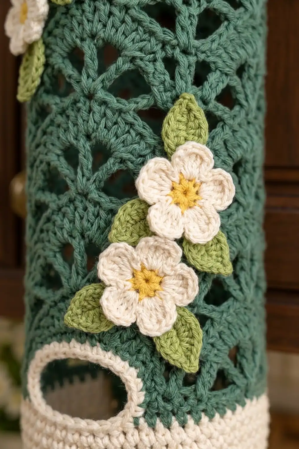 Two white crocheted flowers with golden centers and green leaves on a teal lace-pattern background.