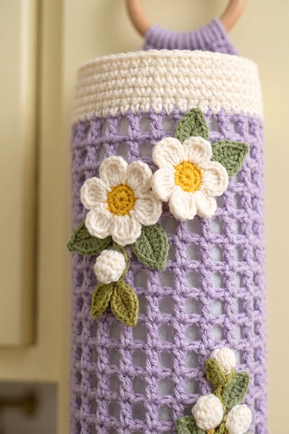 Crocheted lavender basket with cream top, decorated with white daisies featuring golden centers and green leaves.