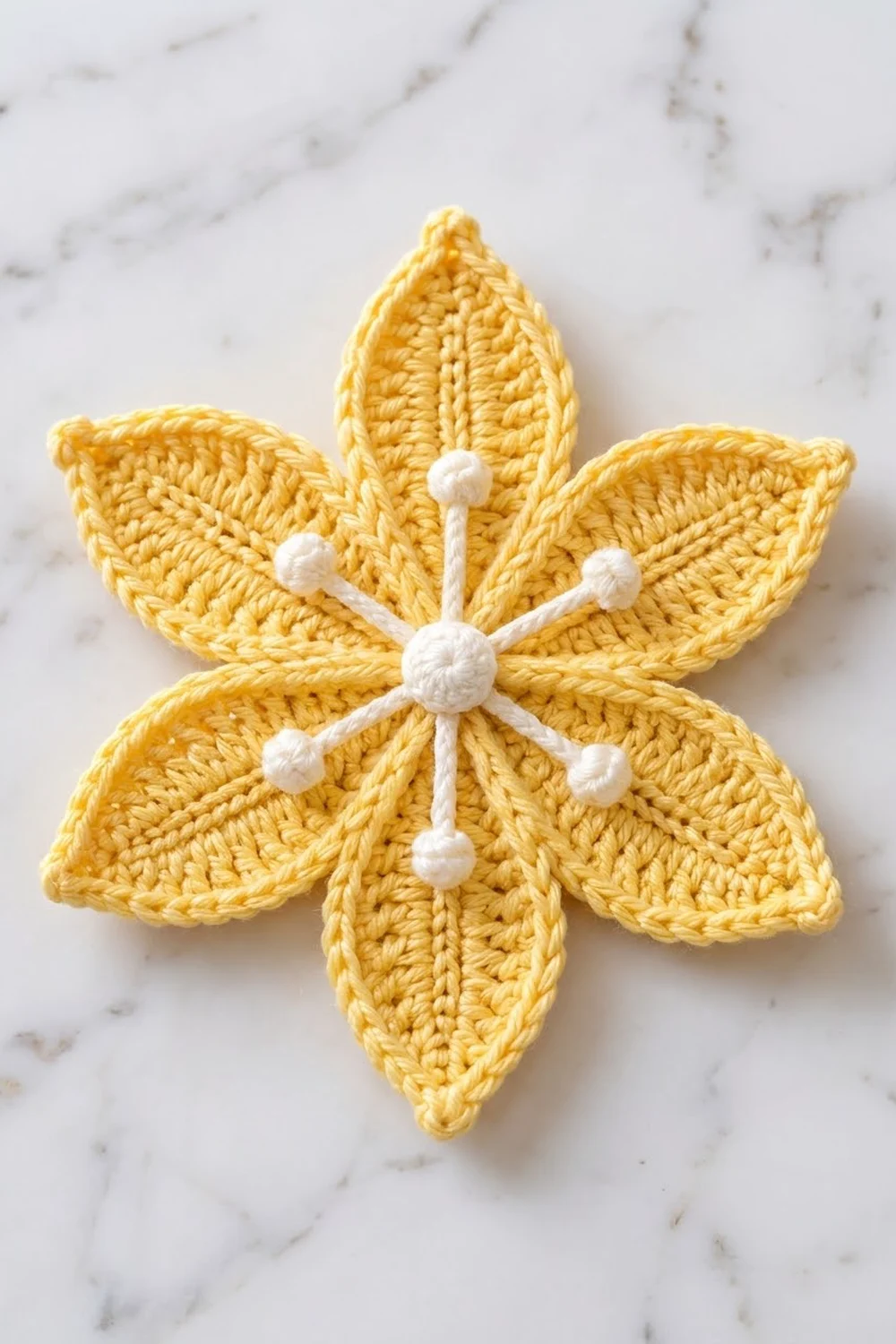 Golden-yellow crocheted five-petal flower with white bead embellishments centered on a marbled gray surface.