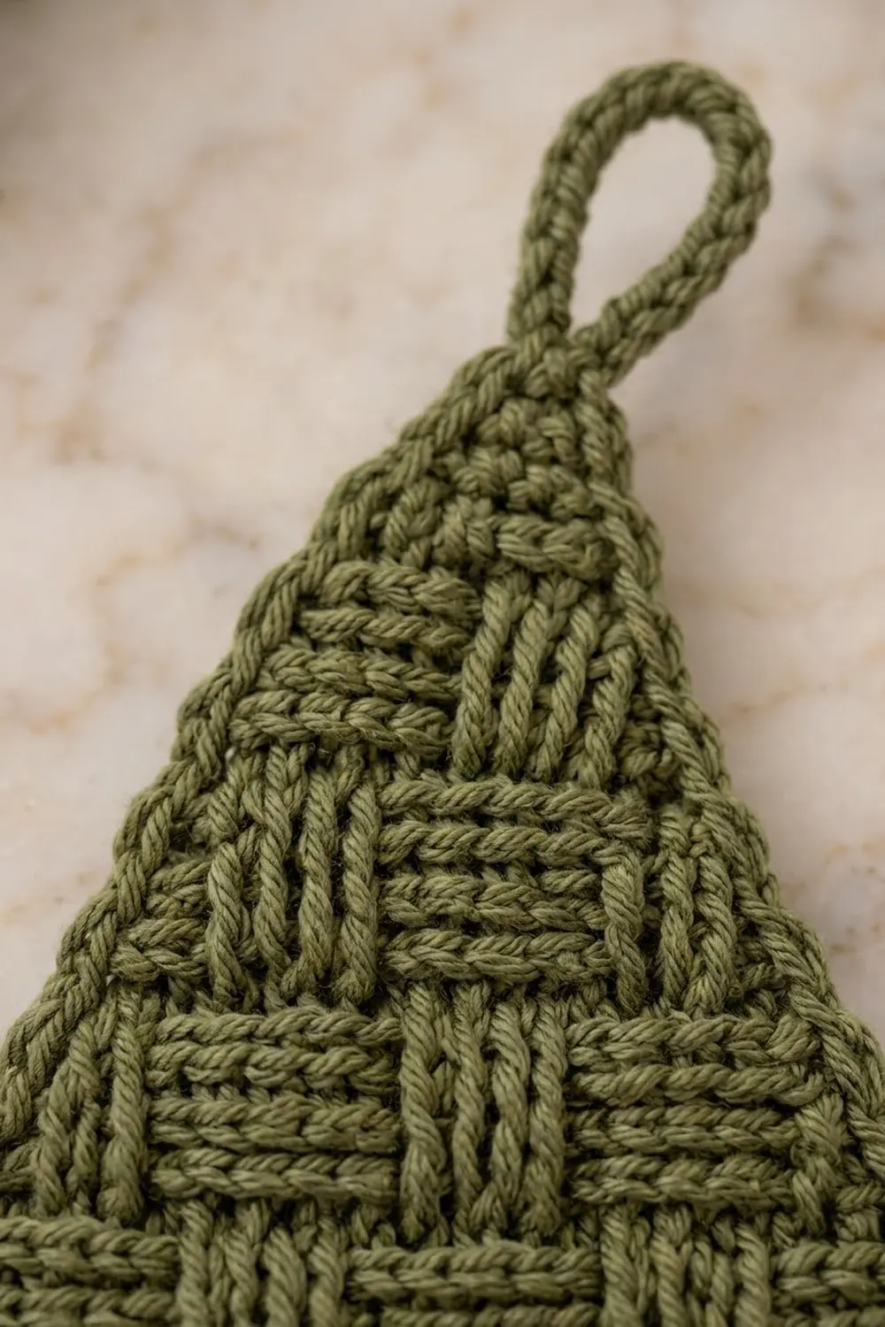 Sage green crocheted pouch with textured basketweave stitching and loop handle against a soft neutral background.