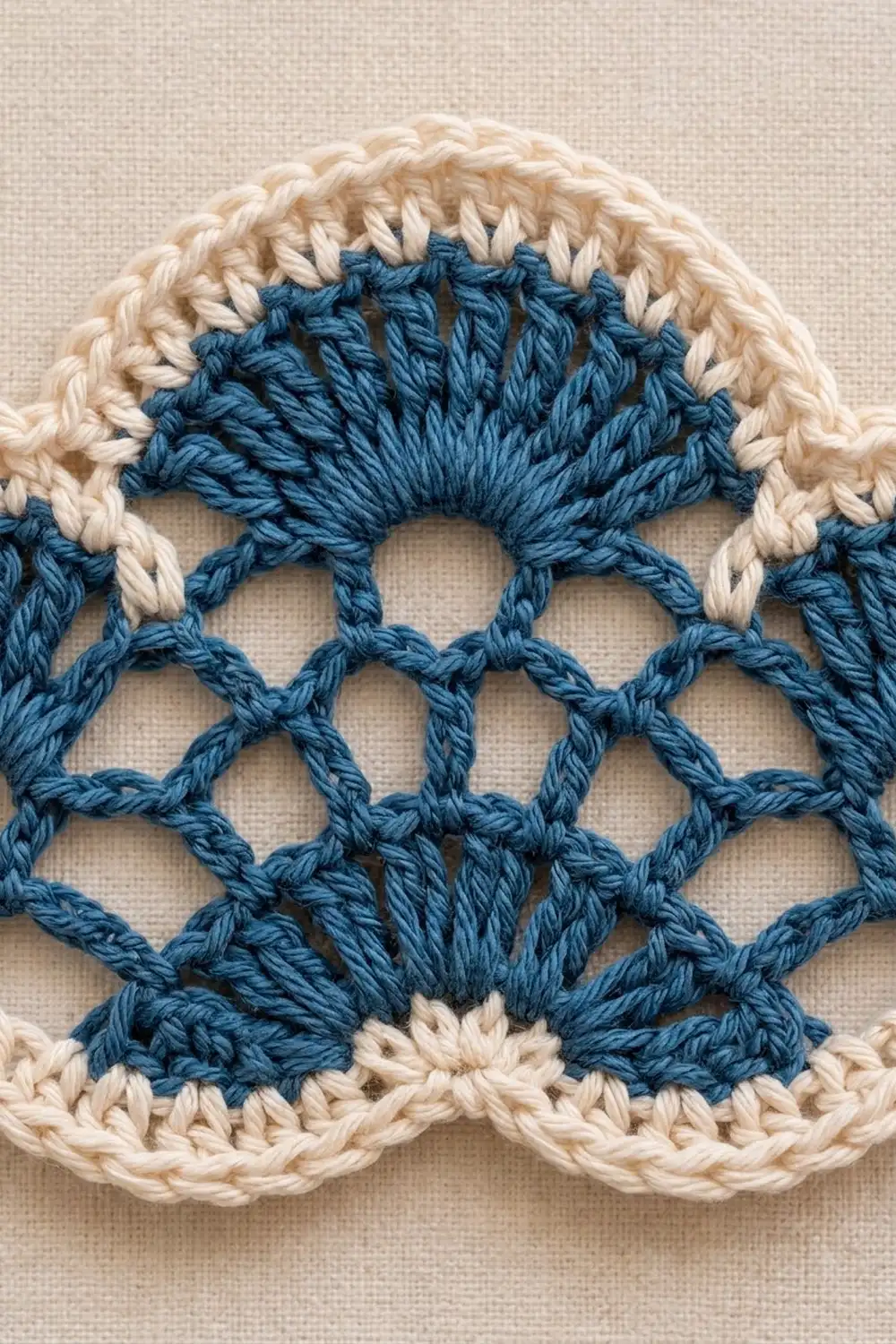 Close-up of crochet featuring cream-bordered, deep teal shell stitches on natural linen fabric.