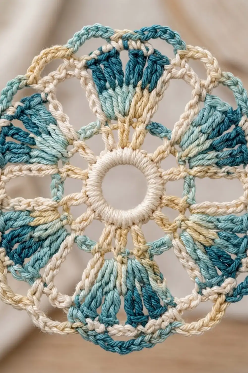 Crocheted doily in teal, cream, and tan with geometric mandala pattern and central opening.