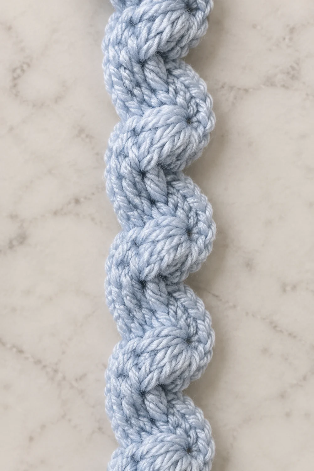 Close-up of a light blue twisted rope with uniform knots displayed vertically on a marble surface.