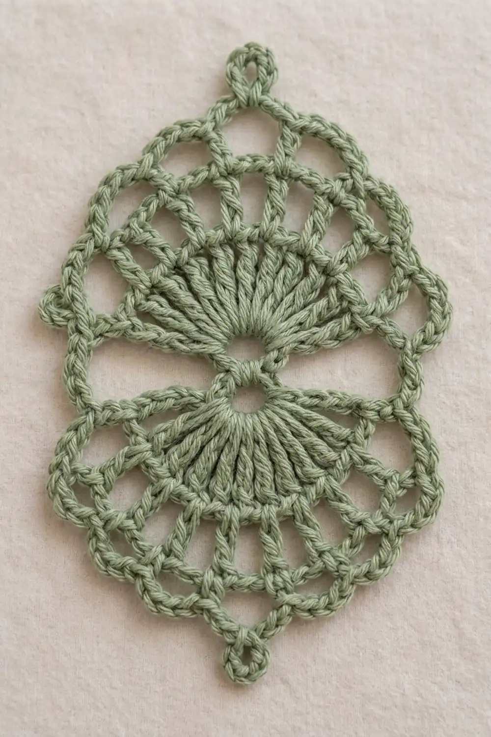 Sage green crocheted ornament with radiating shell stitch fans and geometric openwork pattern on cream linen.