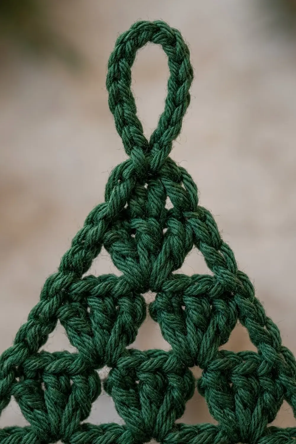 Close-up of thick green crocheted pyramid with twisted yarn loops arranged in geometric layers against soft background.