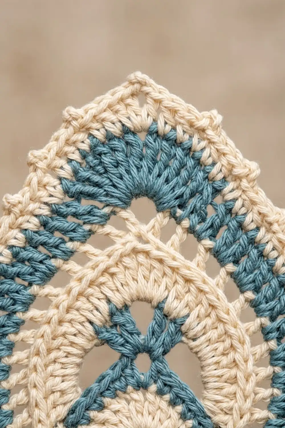 Close-up of interlocking crocheted stitches in cream and teal yarn against a soft, neutral background.