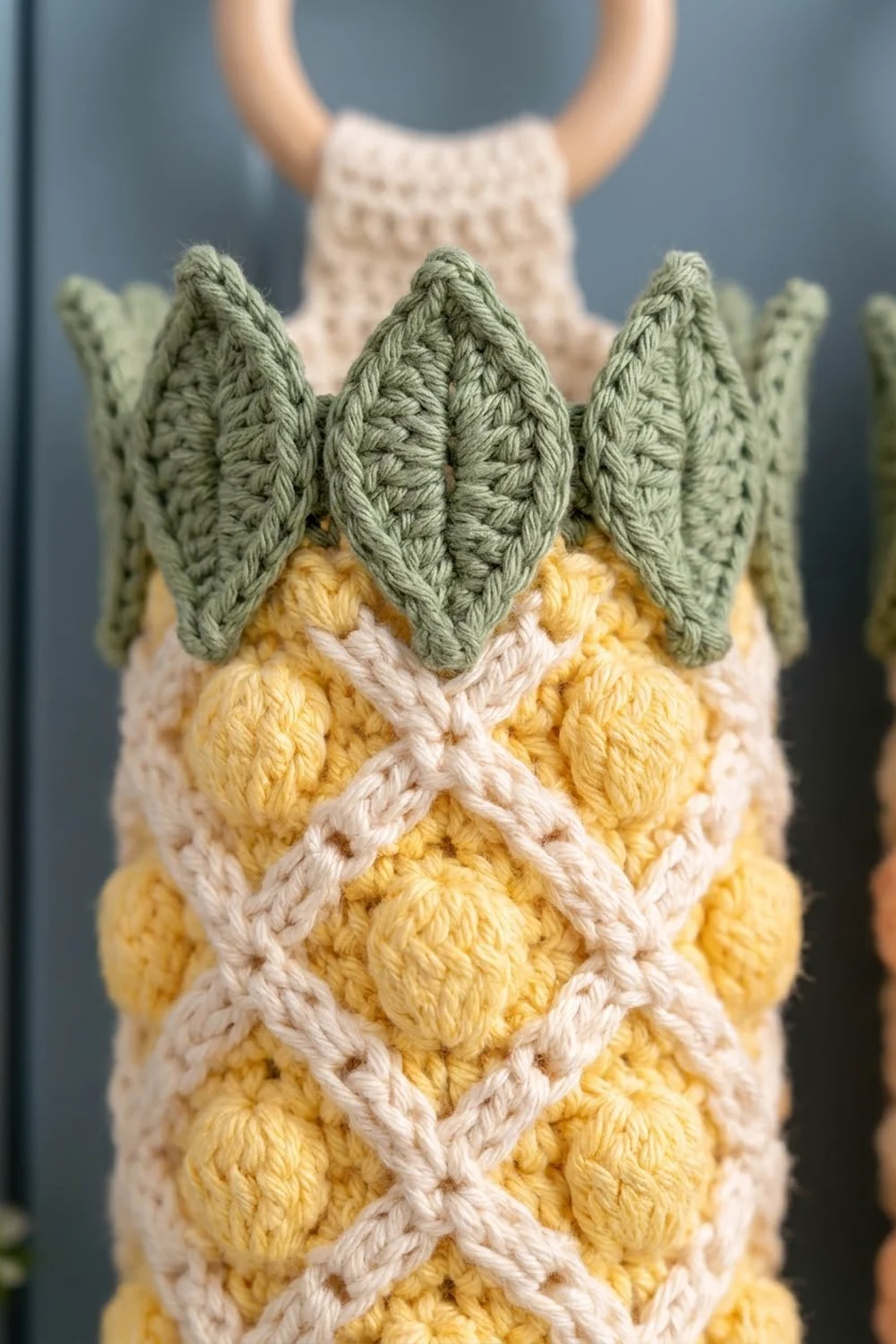 Close-up of a crocheted owl with green leaf ears, yellow and white textured body, and cream wooden bead handle.