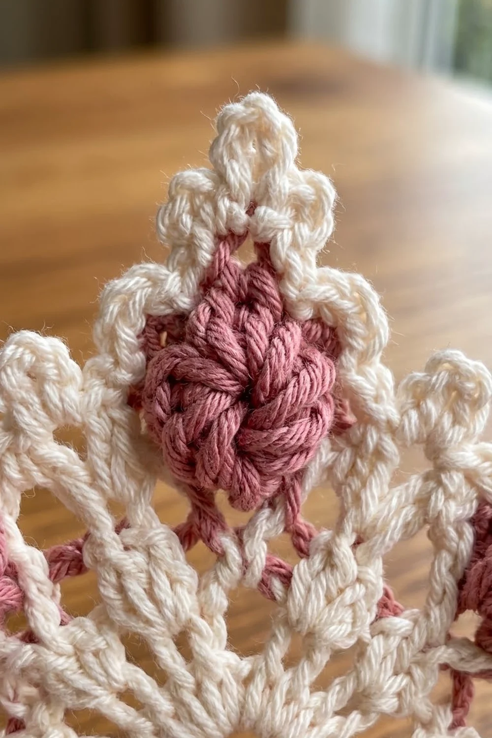 Twisted crocheted strands in cream and rose pink create a detailed, rope-like textured pattern.