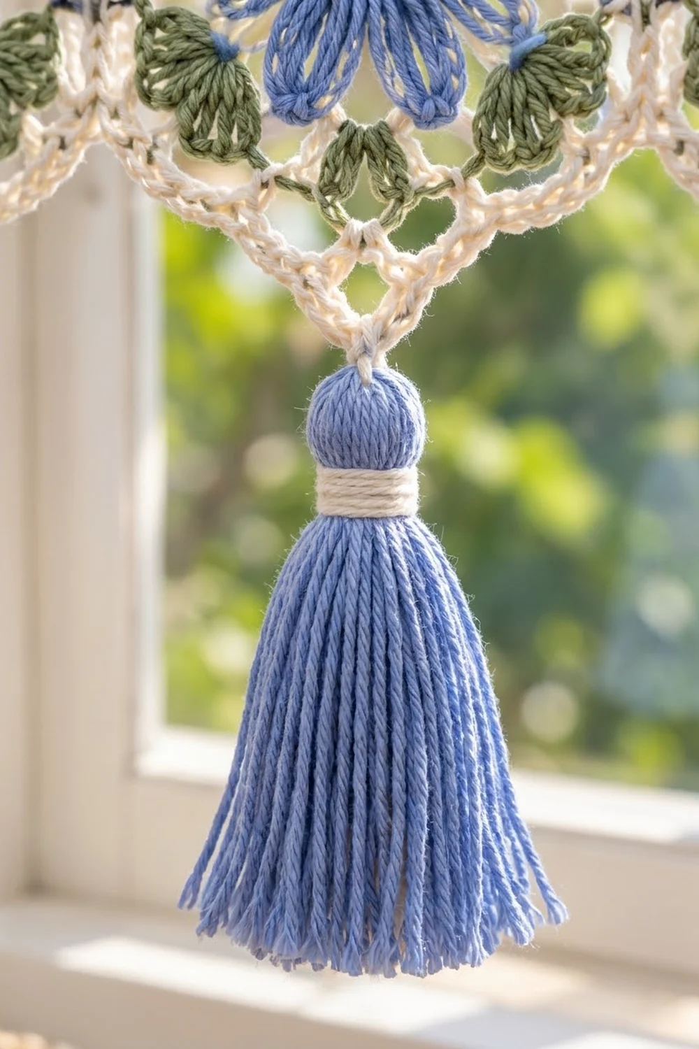 Periwinkle tassel with cream binding and green crocheted leaves on cream lace border, photographed with soft outdoor background.