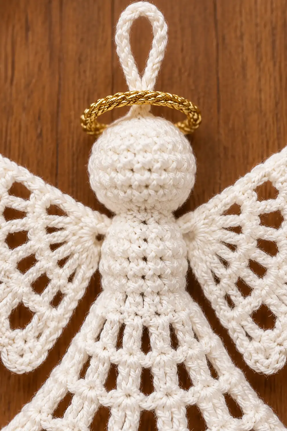 Handmade crocheted white angel ornament with gold halo and lace wings on wooden background.
