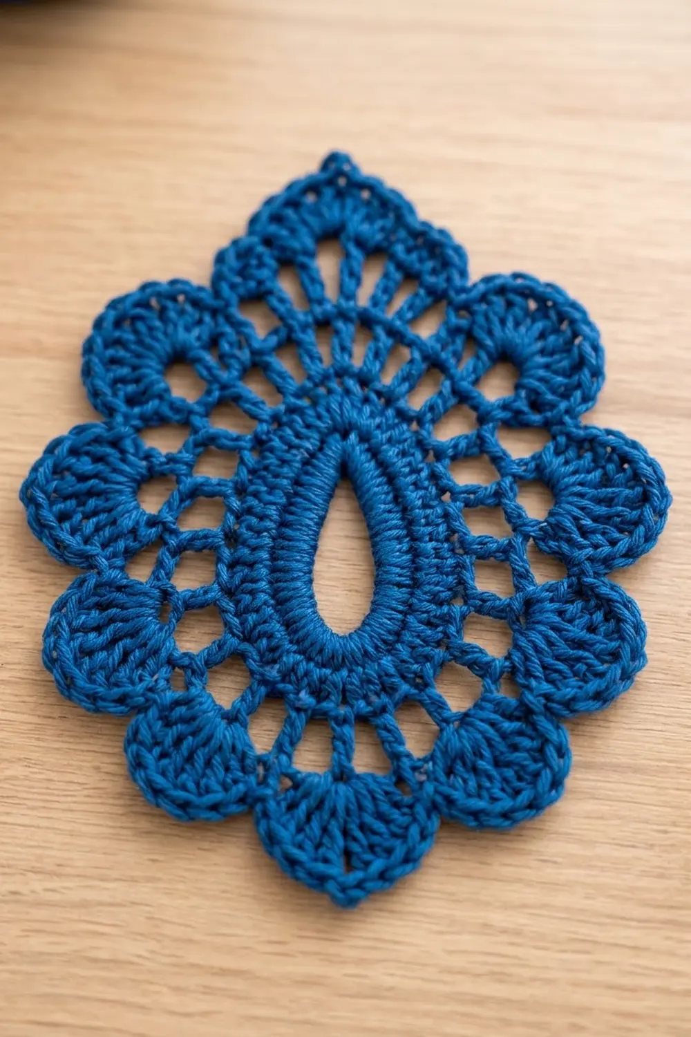 Bright blue crocheted flower with scalloped petals and open lacework detail displayed on a light wooden surface.