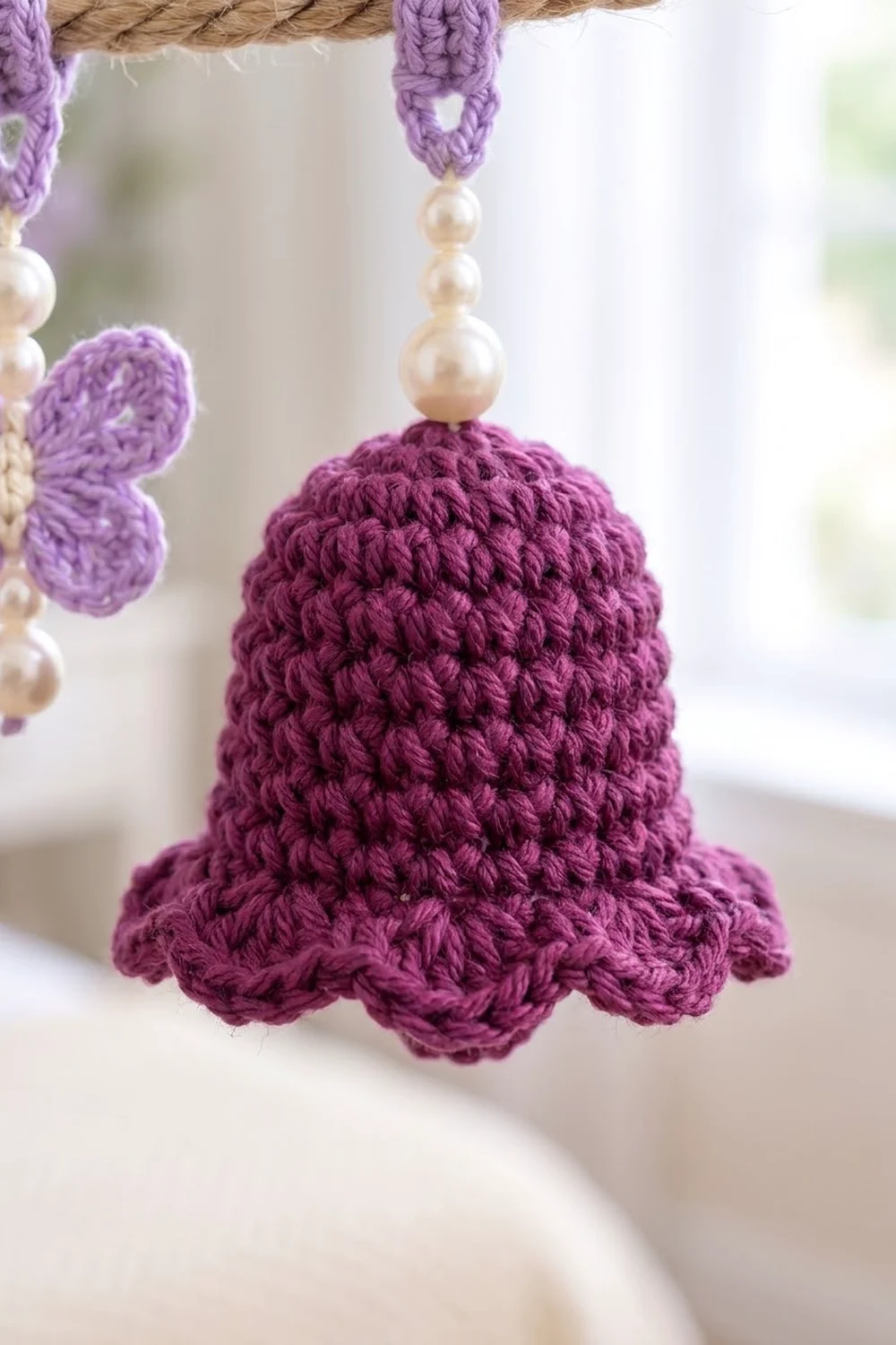Handmade purple crocheted bell with pearl bead drops and scalloped edge, hung from rope.