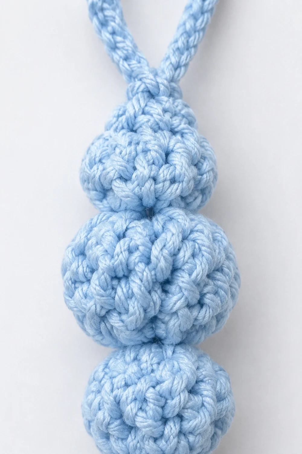 Close-up of a light blue rope toy with three knotted spheres stacked vertically against a white background.