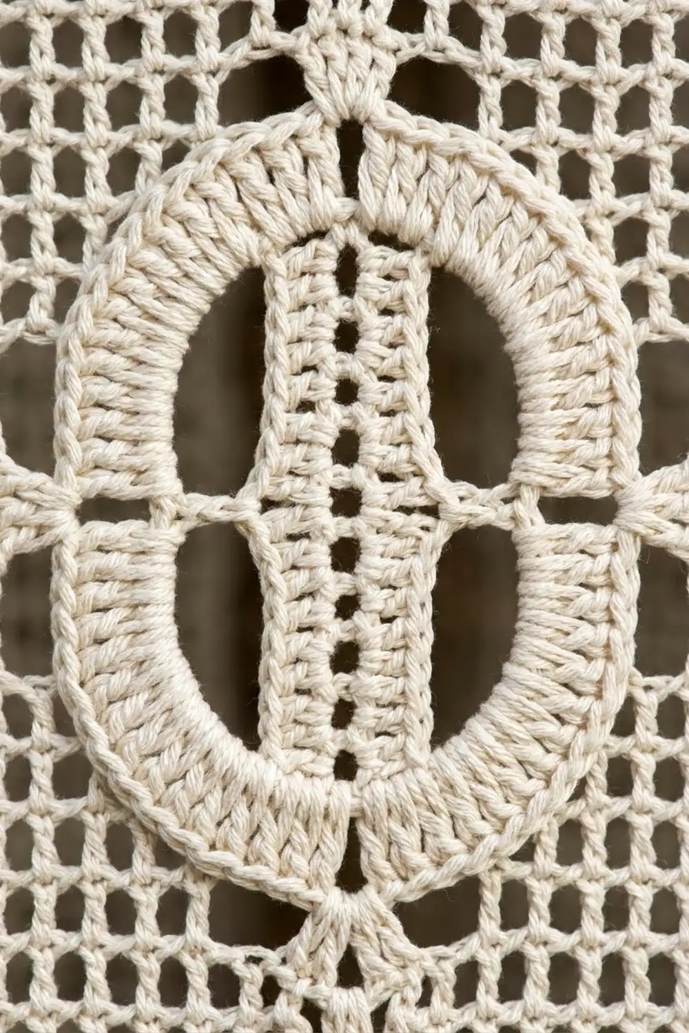 Close-up of cream-colored crocheted lace with layered oval openwork and intricate geometric stitch pattern.
