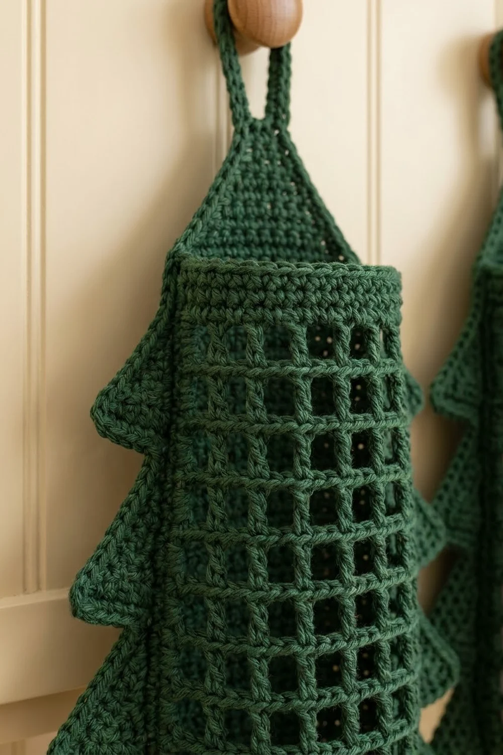 Forest green crochet tower with intricate mesh stitch detail and wooden bead top on cream background.