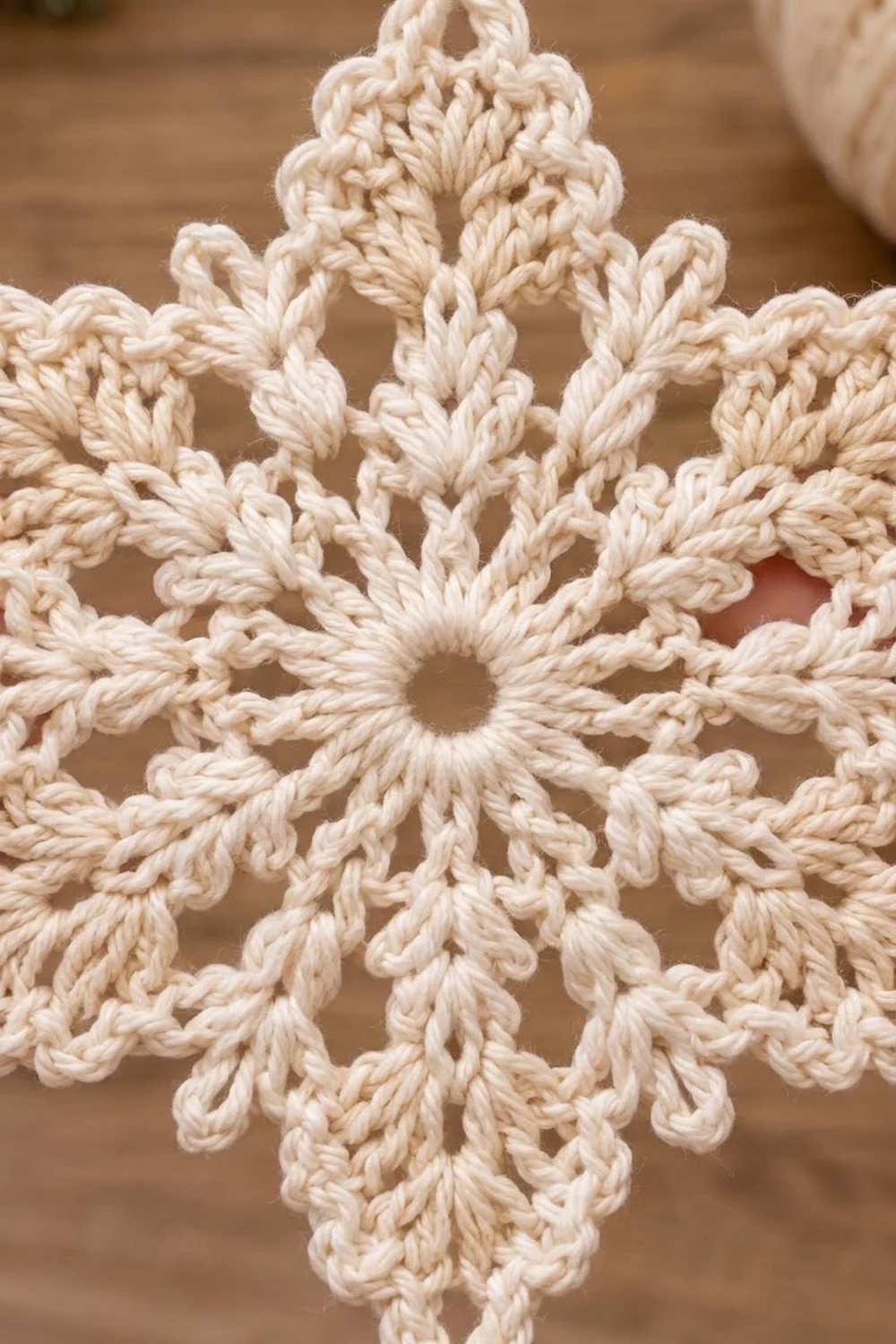 Cream crocheted snowflake with twisted rope stitches and eight-pointed symmetry against a blurred wooden background.