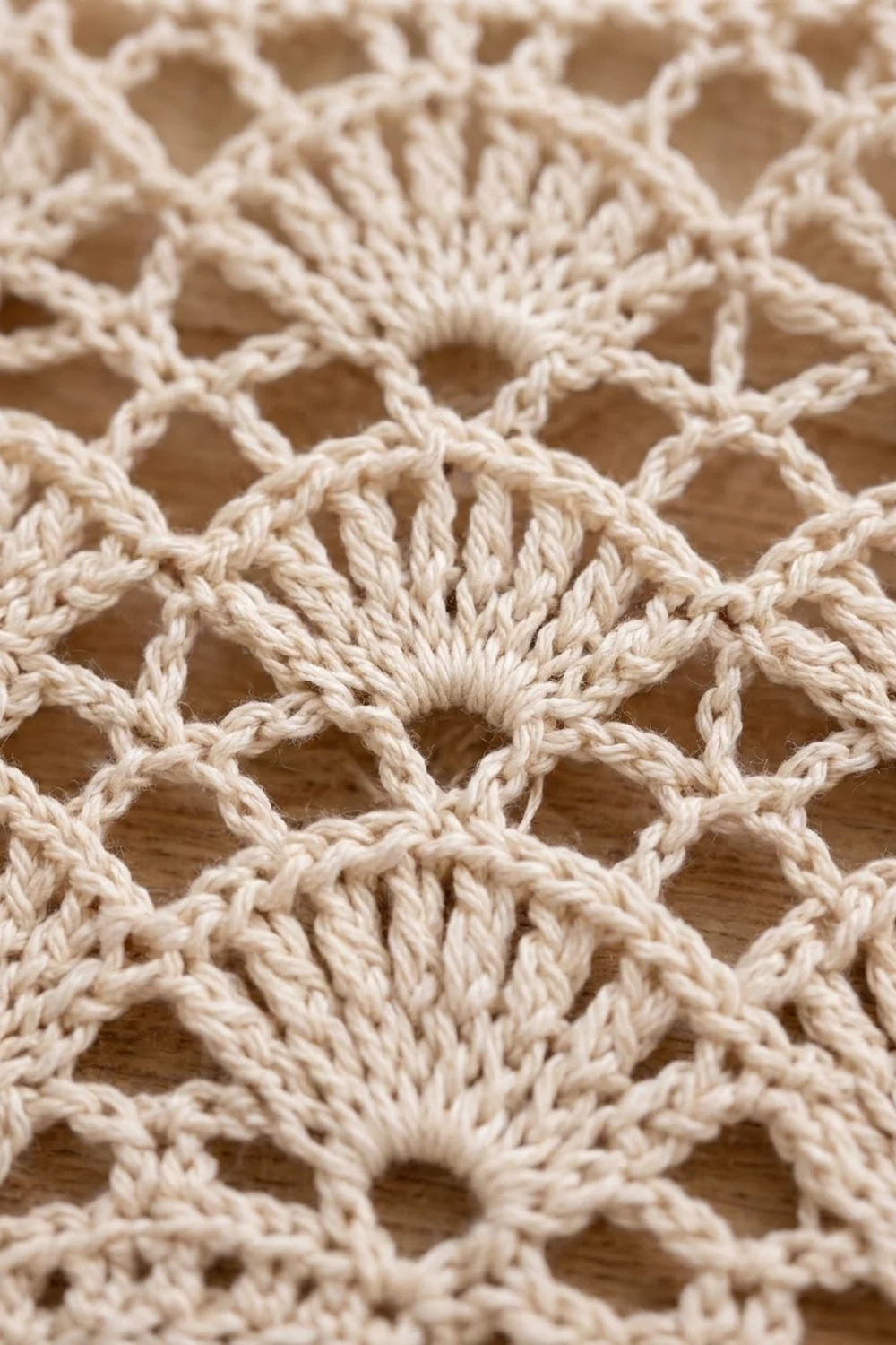 Close-up of cream-colored crochet with an open mesh pattern and textured stitches displayed on a wooden surface.