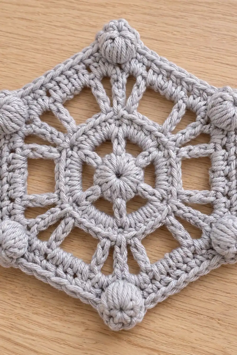 Gray crocheted snowflake ornament with geometric lattice pattern displayed on light wood surface.