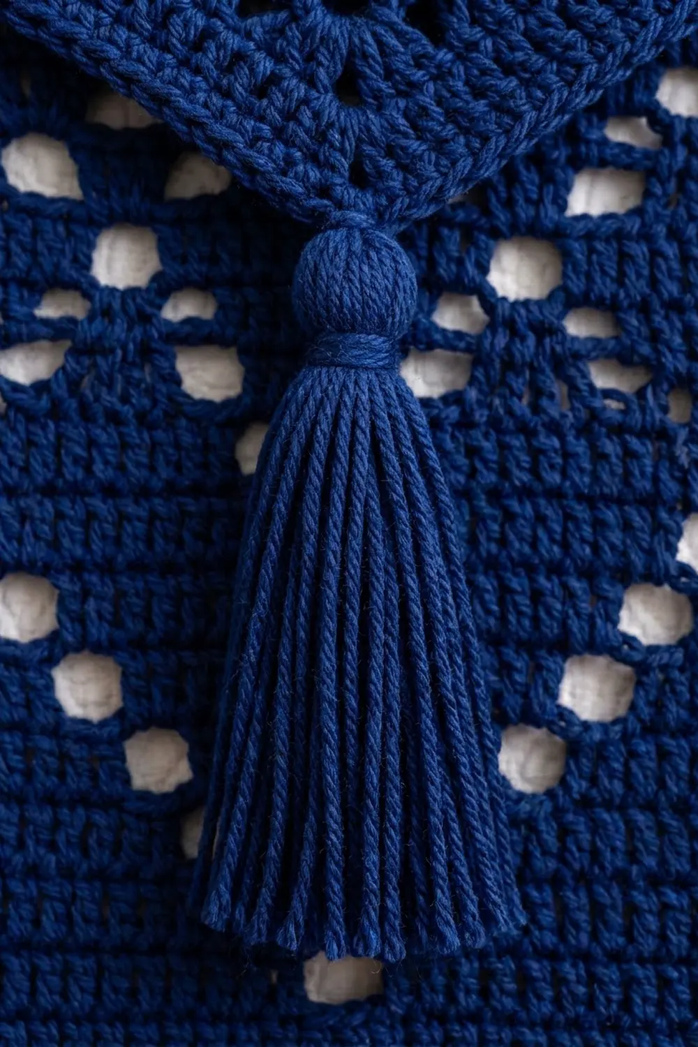 Deep blue crocheted fabric features cream-colored openwork pattern with a centered blue yarn tassel.