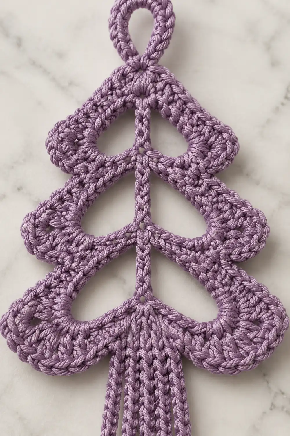 Purple crocheted Christmas tree ornament with scalloped tiers displayed on a marble surface.