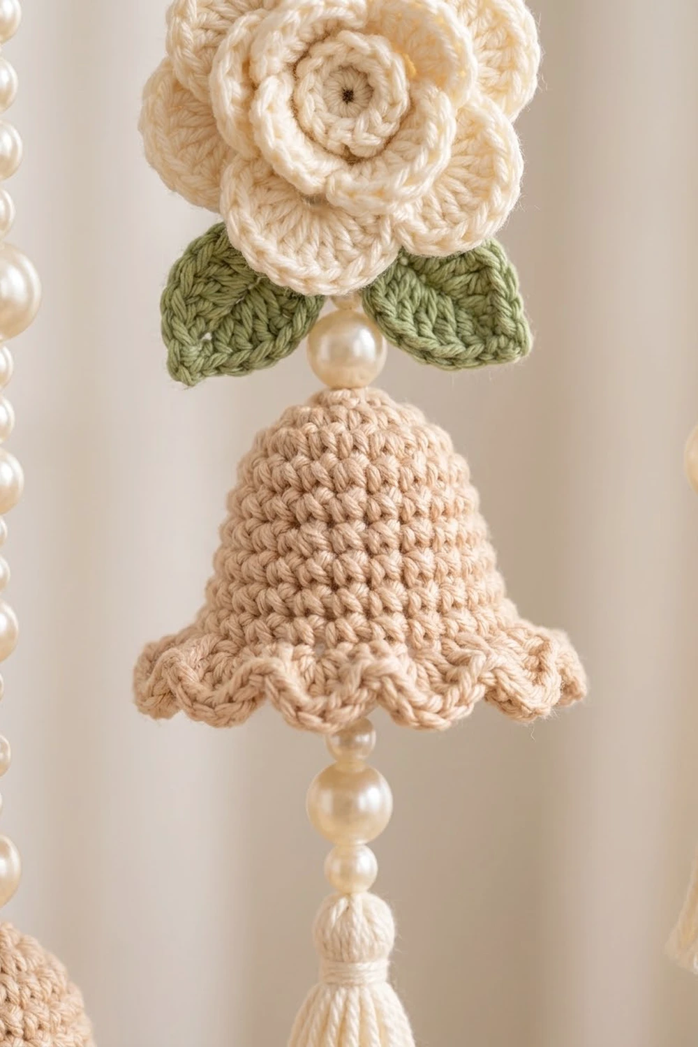 Close-up of crocheted cream rose and bell ornament with green leaves and pearl bead accents.