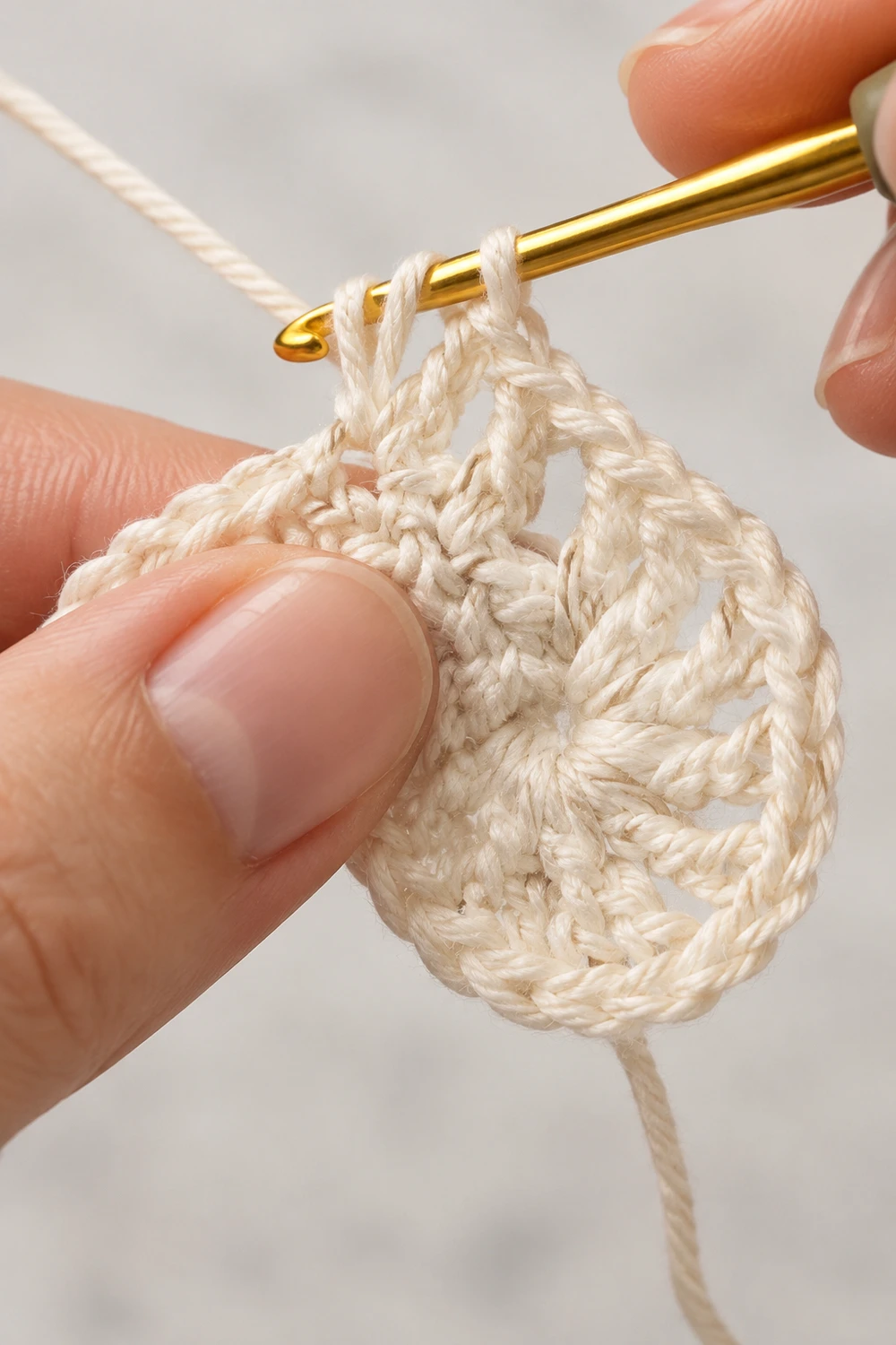 Close-up of cream-colored crochet stitches on a gold hook held between fingers against a light background.