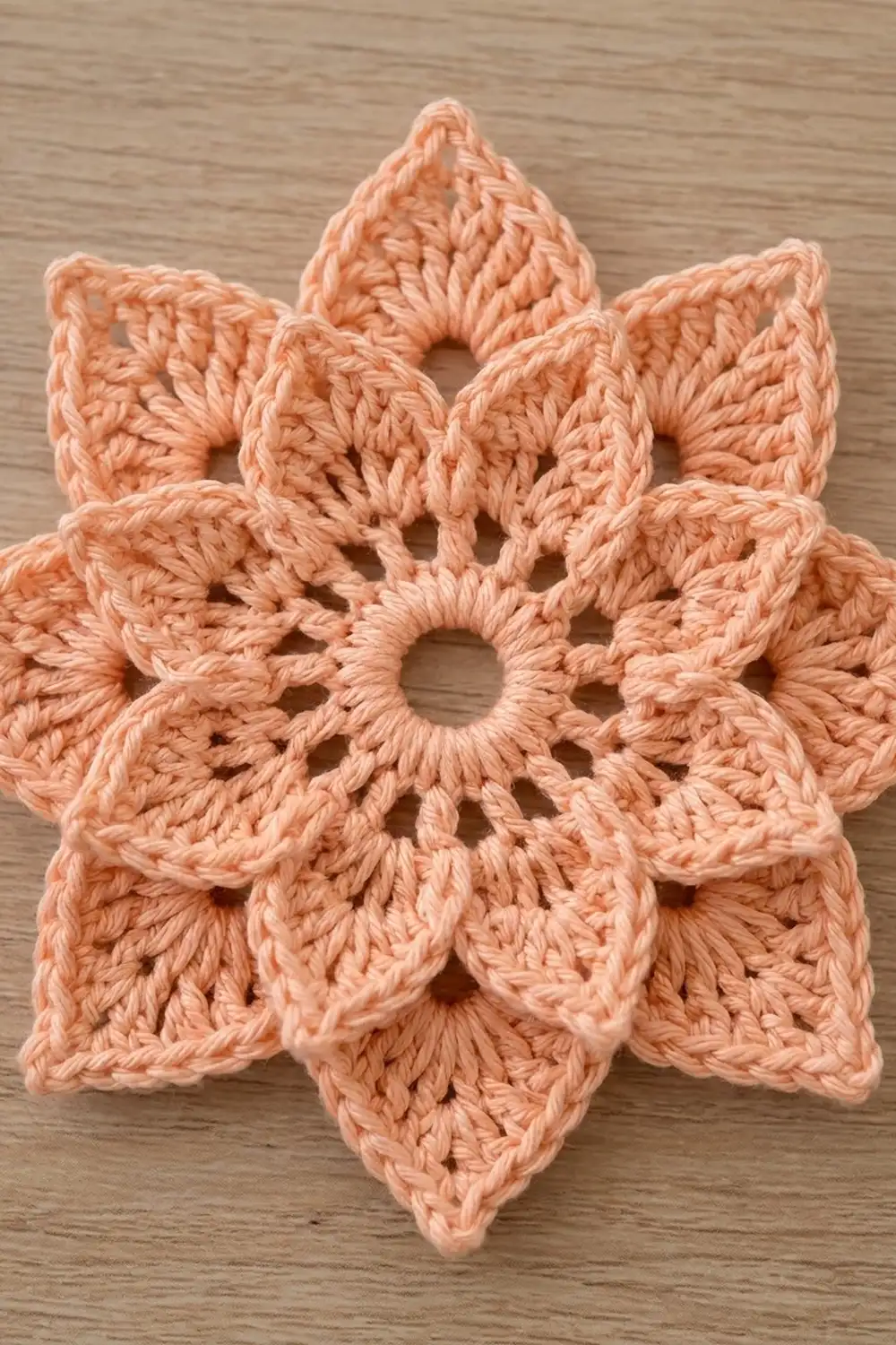 Close-up of peachy-salmon crocheted flower with openwork lace detail on natural wood surface.