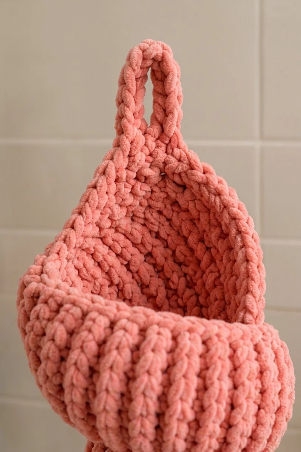 Close-up of a coral-pink crocheted bag with textured popcorn stitches and braided handles.