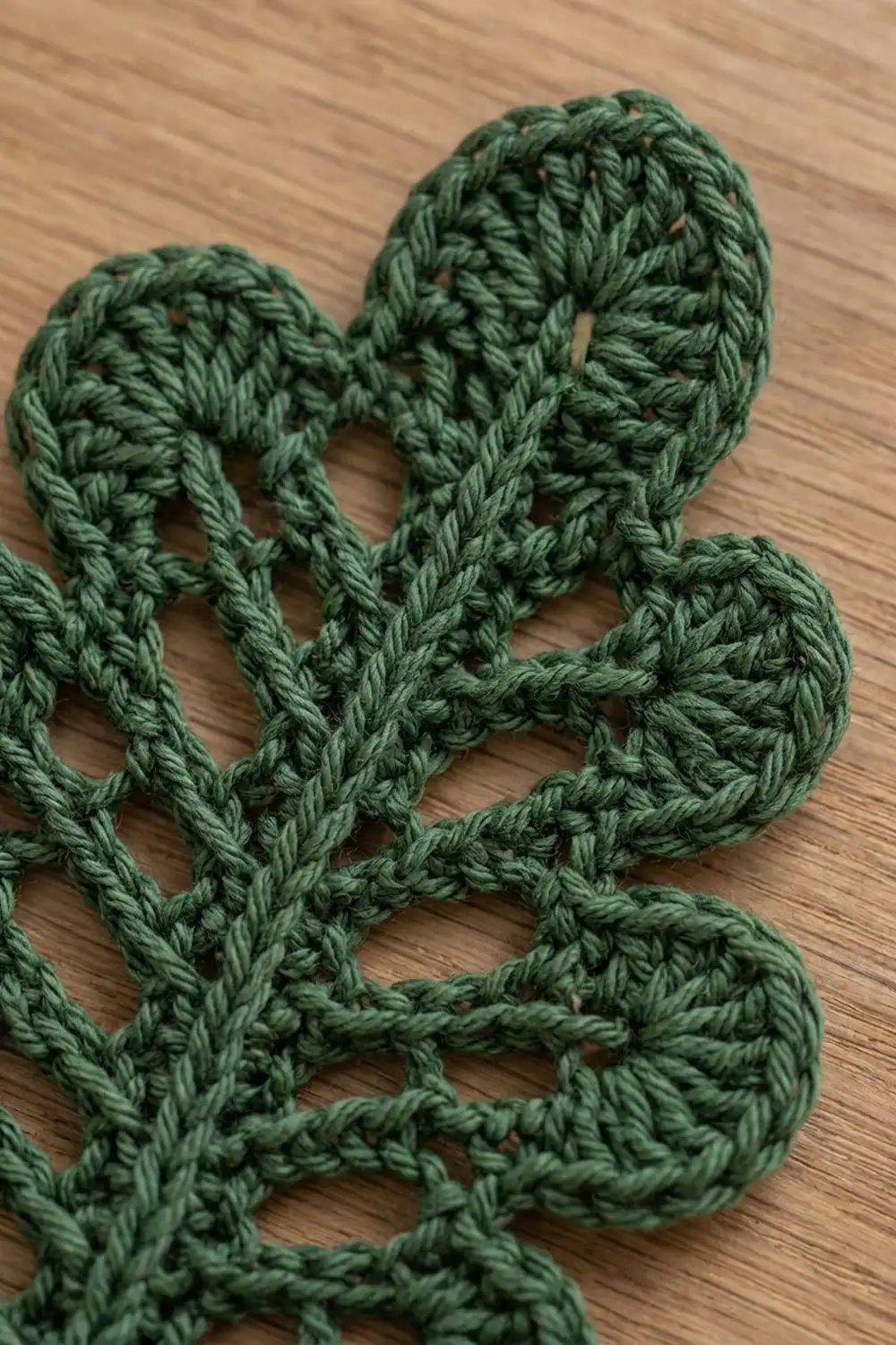 Sage green crocheted cactus motif with scalloped-edge details on a light wood surface.