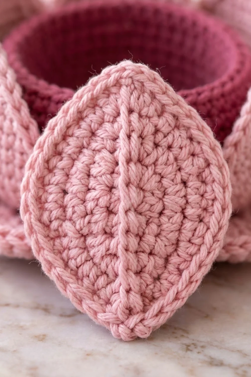 Close-up of a hand-crocheted pink egg showing detailed stitch texture on a neutral surface.