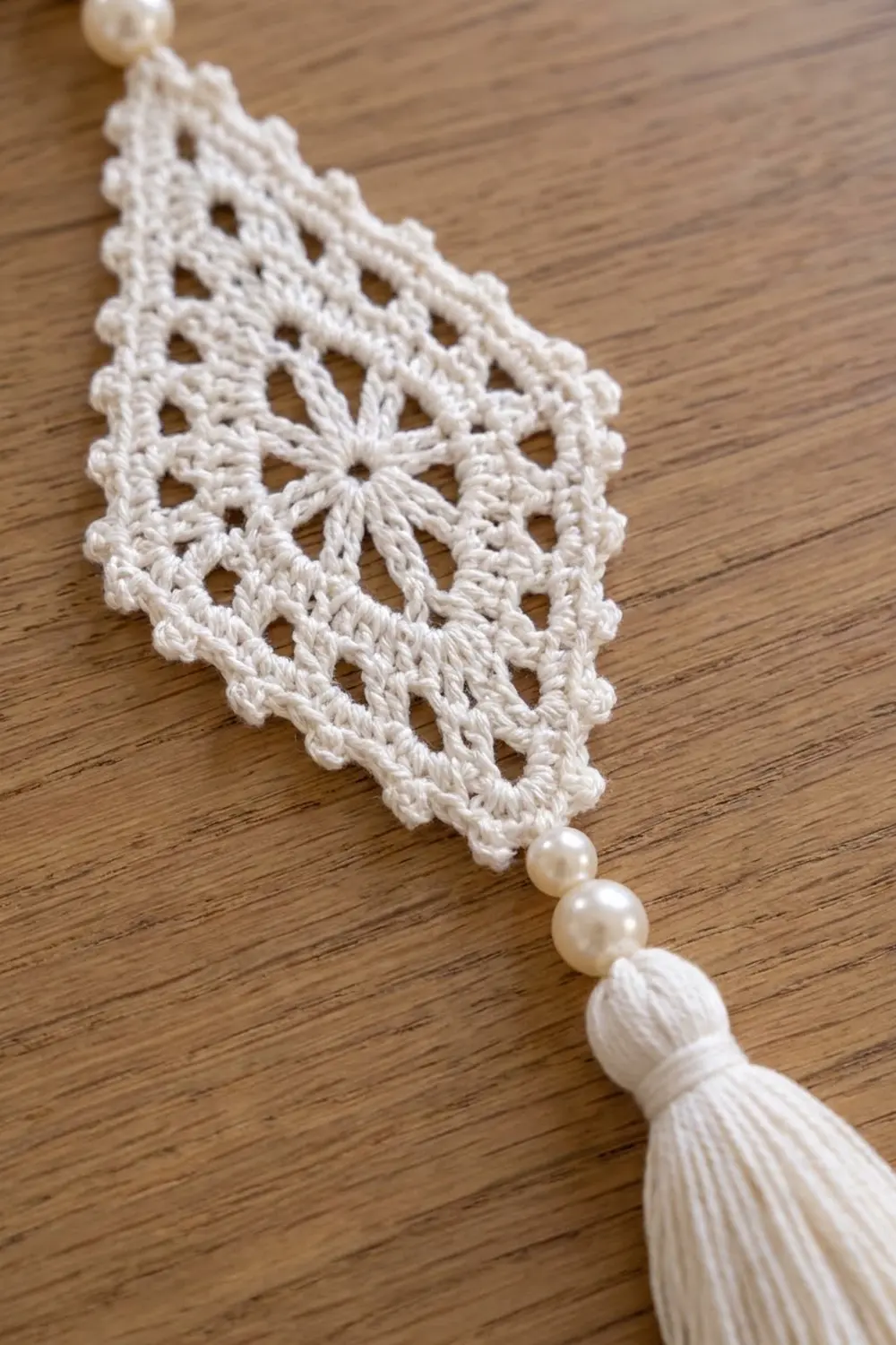 White crocheted lace with openwork pattern and beaded pearl tassel on warm wooden surface.