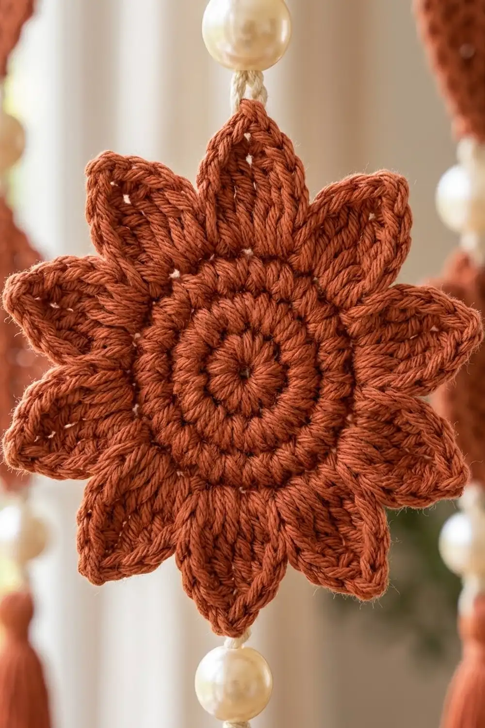 Rust-toned crocheted snowflake with pearl bead caps positioned among similar handmade ornaments in soft, warm lighting.
