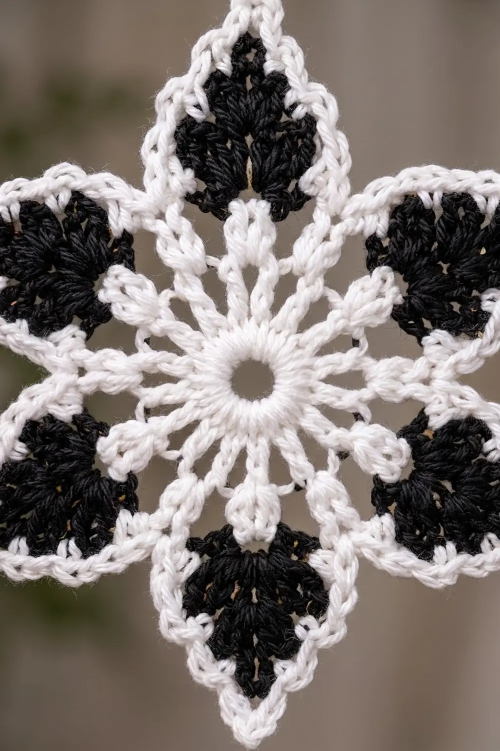 Close-up of a crocheted snowflake ornament in black and white yarn with intricate six-point symmetrical design.