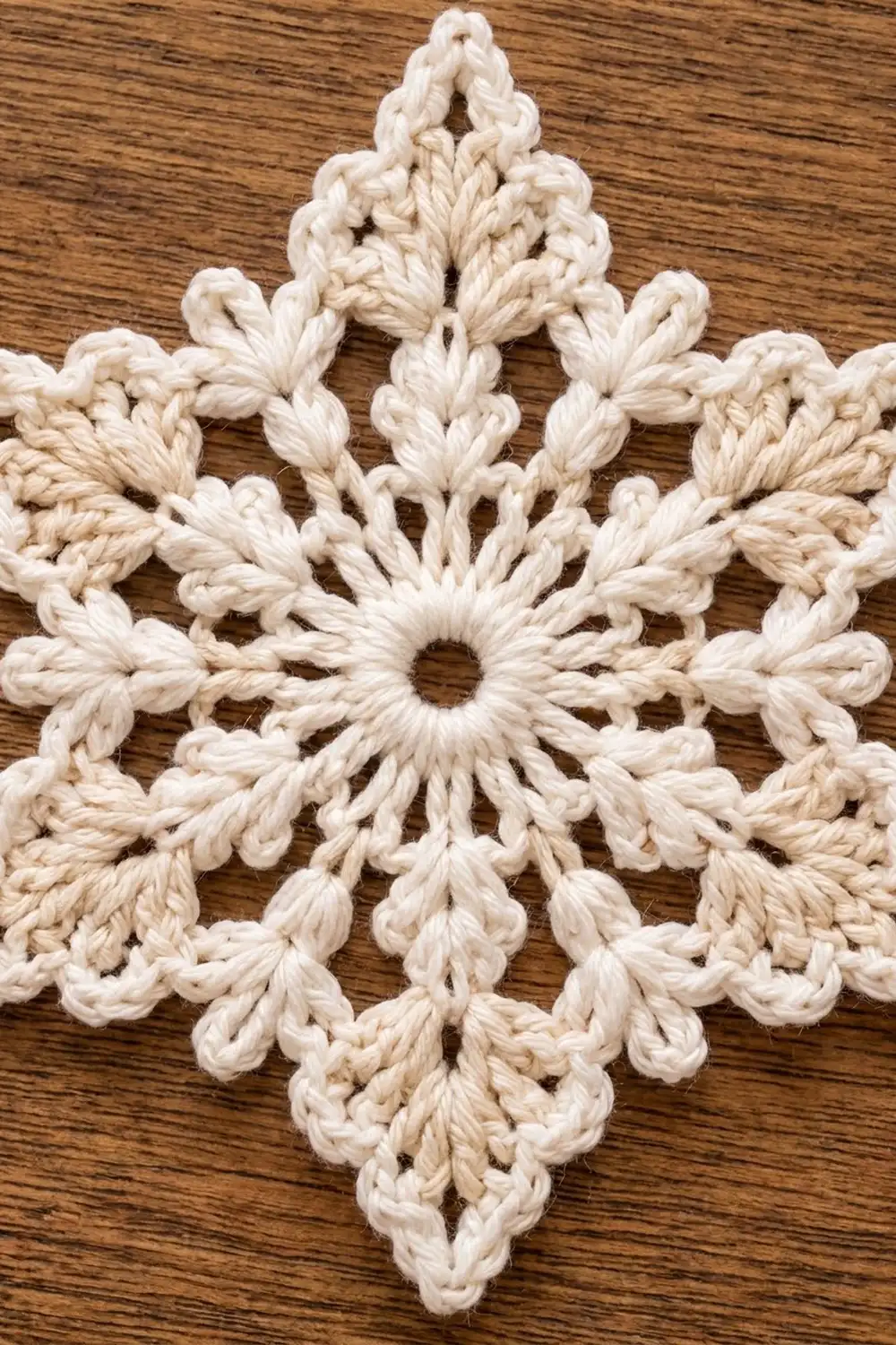 Handmade cream-colored crocheted snowflake with detailed looped petals resting on dark wood grain.