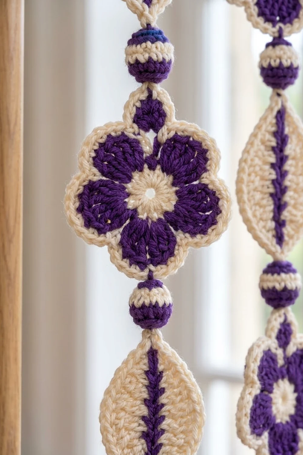 Handcrafted crochet flower ornament with purple petals and cream center suspended near a bright window.