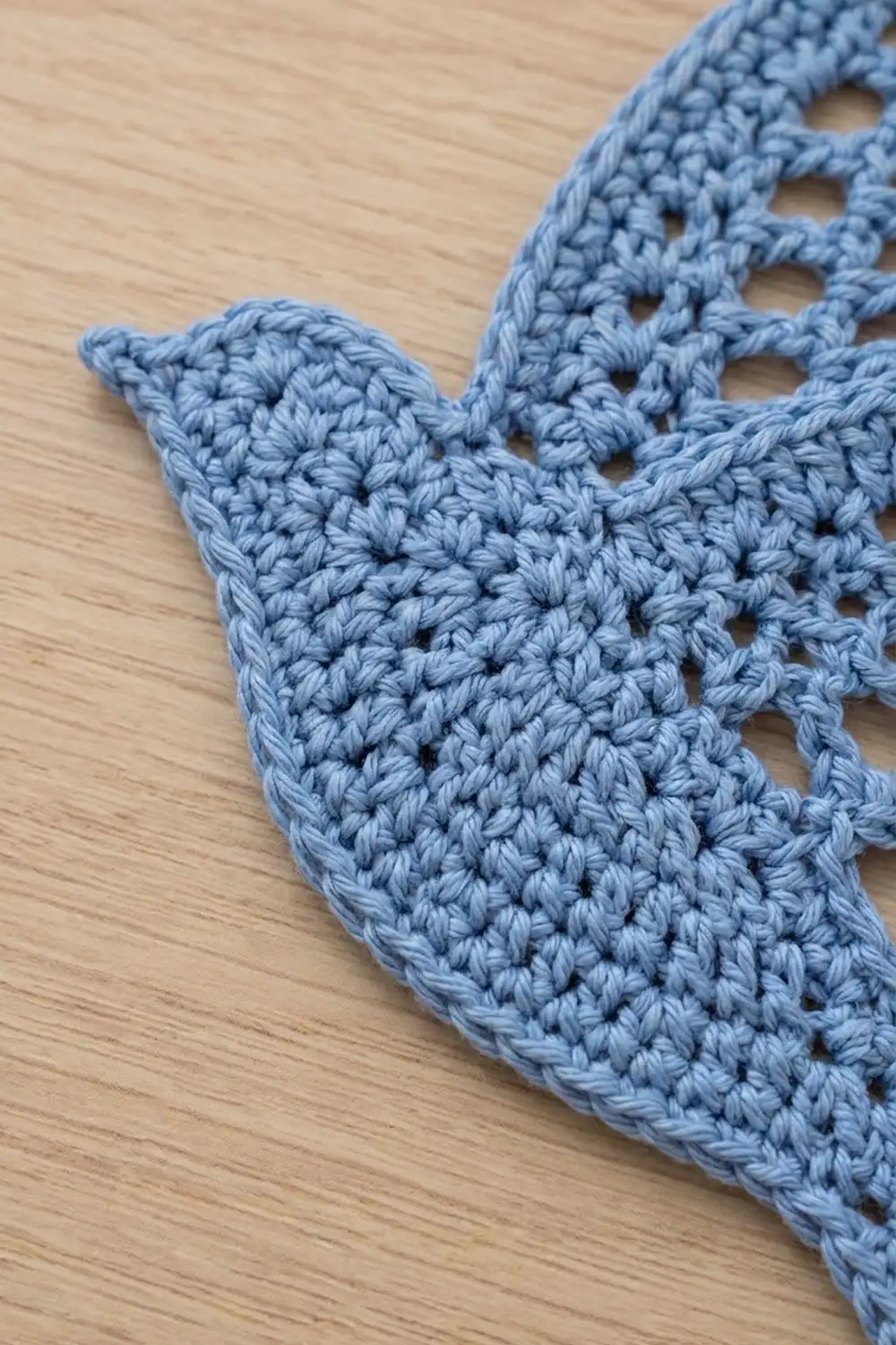 Light blue crocheted fabric with delicate openwork stitches resting on natural wood.