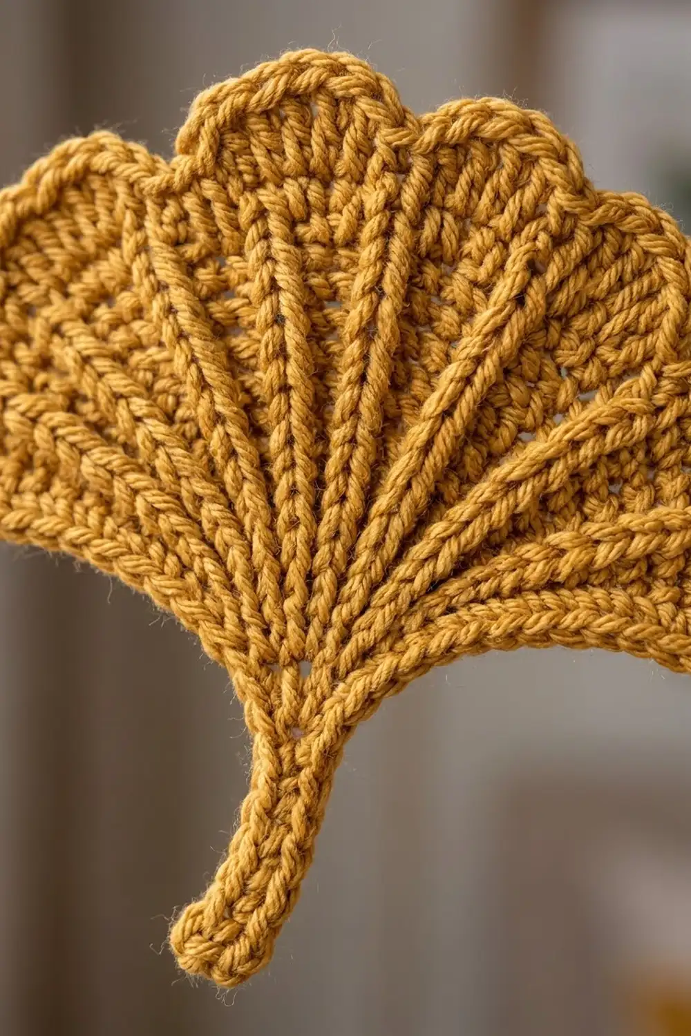 Golden-yellow crocheted heart displaying intricate cable stitch texture, photographed in close-up against a blurred background.