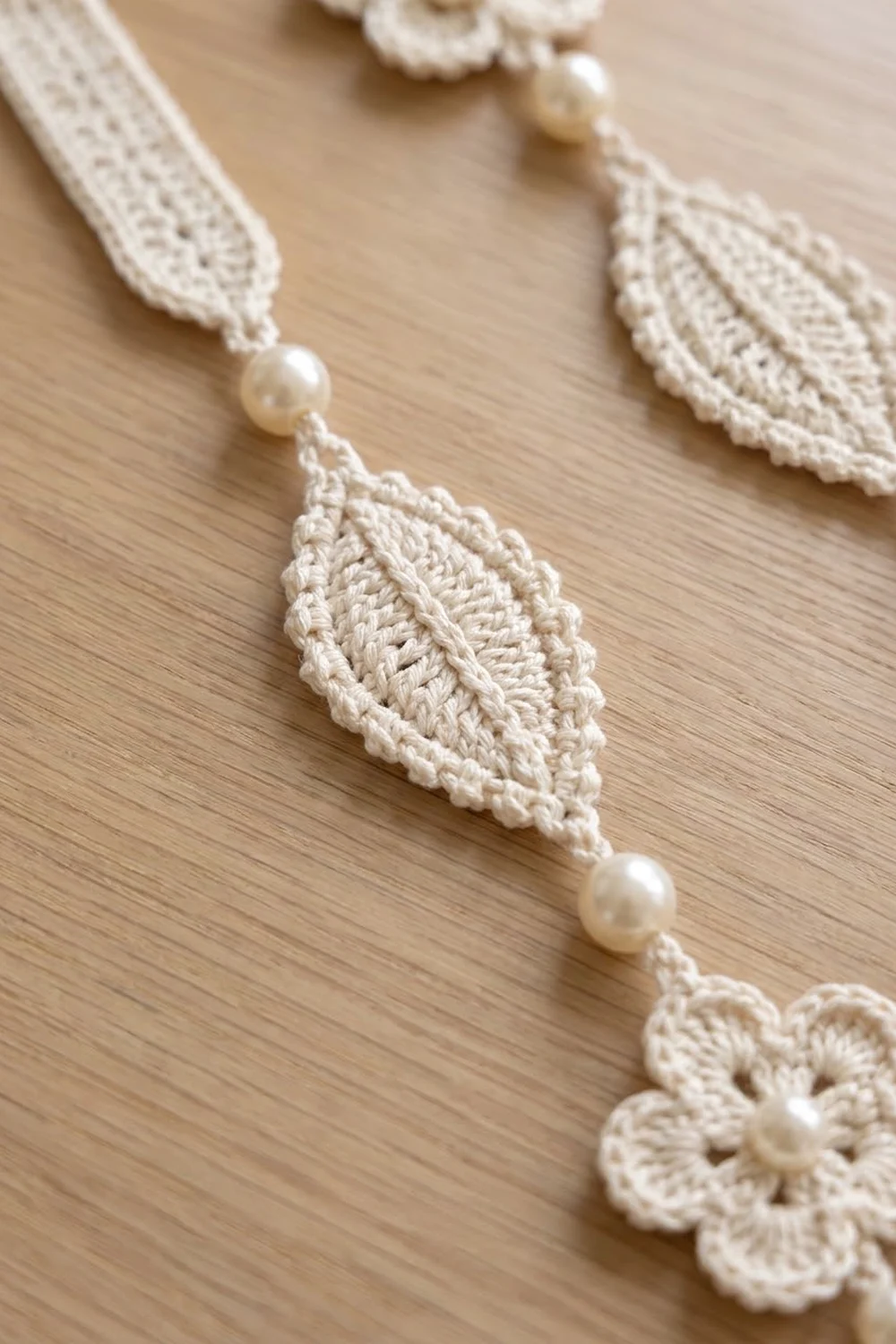 Cream crocheted necklace with leaf-shaped elements and pearl beads displayed on light wood.