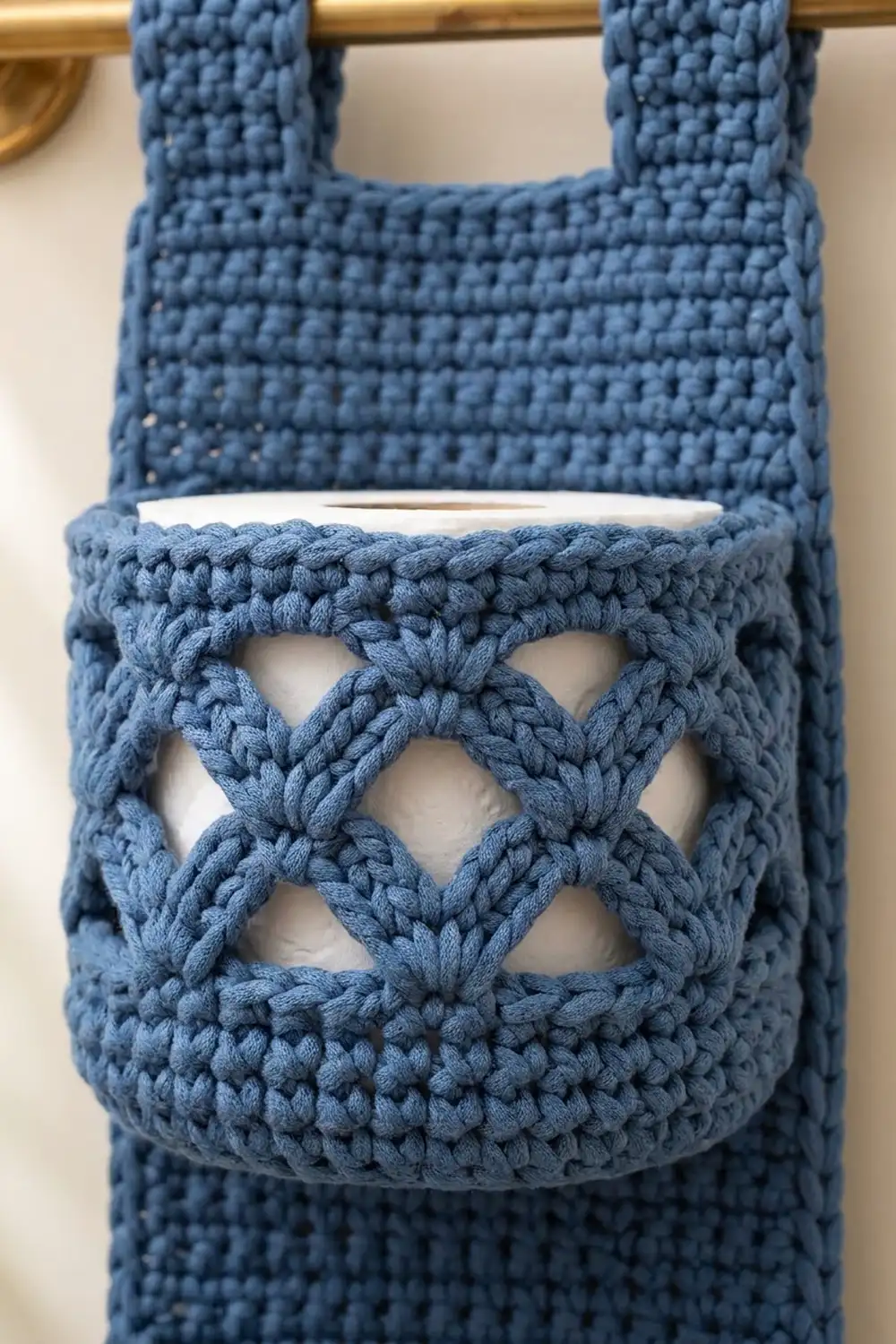 Close-up of a blue crocheted bag featuring an open diamond lattice pattern, suspended from a gold-toned rod.