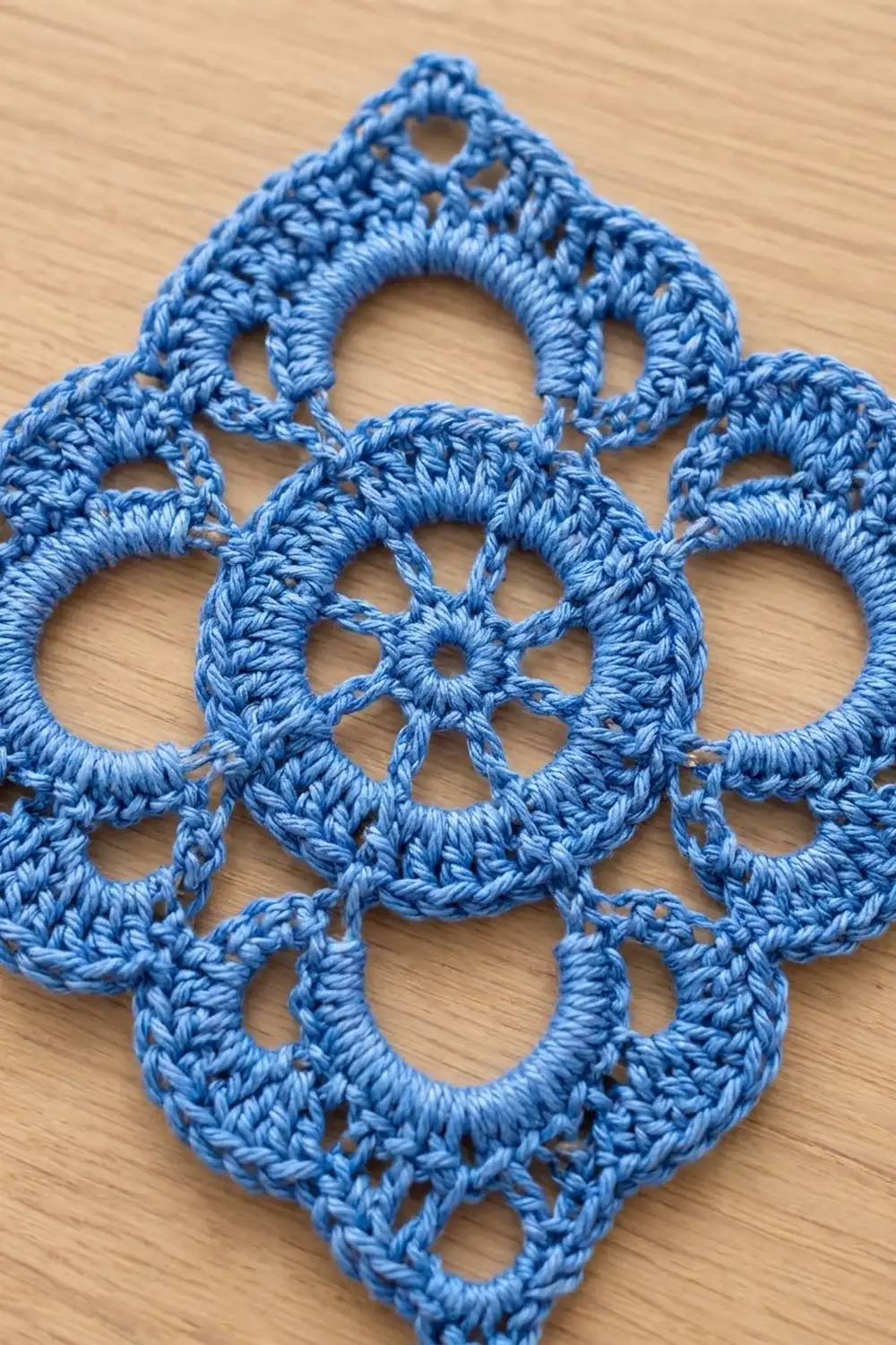 Close-up of a bright blue crocheted lace pendant with intricate geometric holes on a natural wood surface.