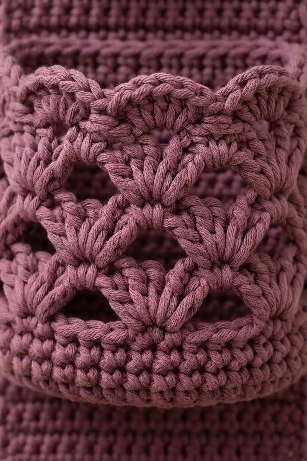 Close-up of dusty rose crochet showing intricate looped stitches with decorative openwork diamond patterns.
