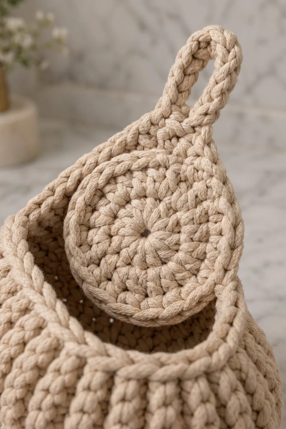 Cream-colored crocheted pouch with braided rope handle, close-up detail showing intricate stitch texture against soft background.