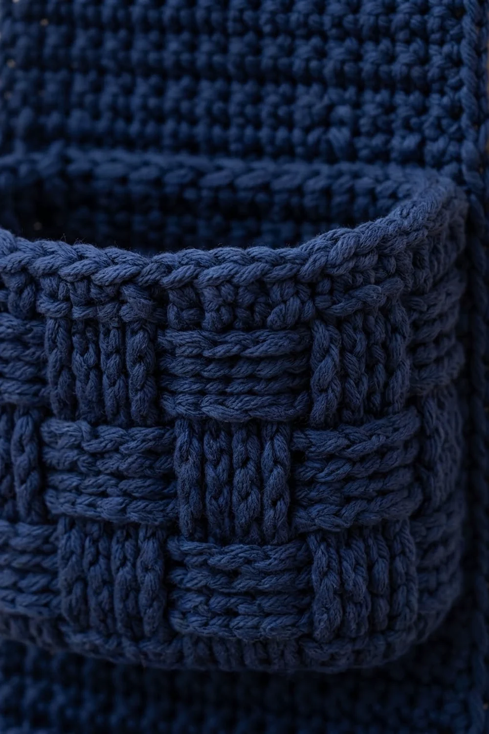 Close-up detail of navy blue knitted fabric revealing layered cable knit texture and stitch pattern.