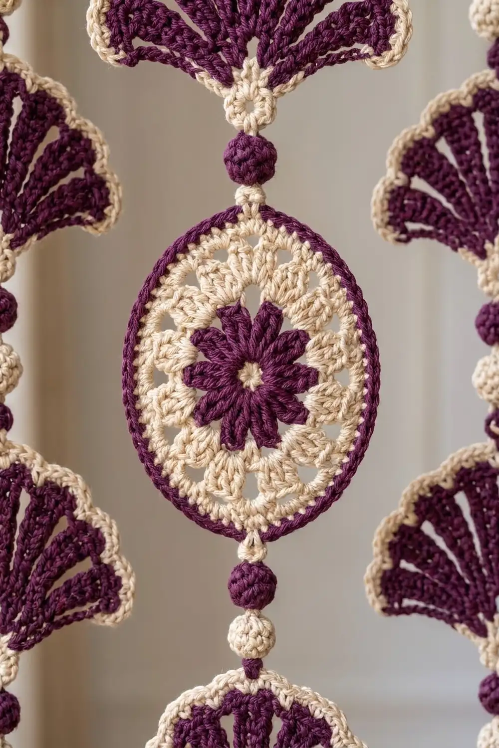 Close-up of intricate crocheted doily with purple and cream oval medallions featuring central floral motifs on neutral background.