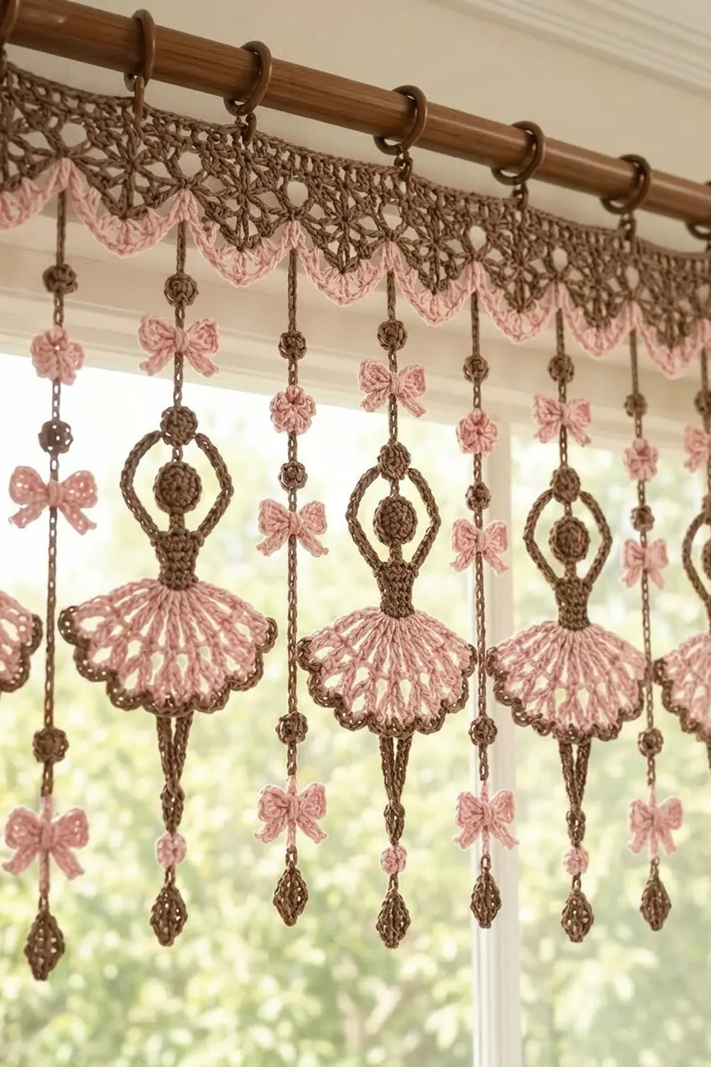 Crocheted window curtain with brown lacy border and hanging pink ballet dancers with bow accents, backlit by a window.