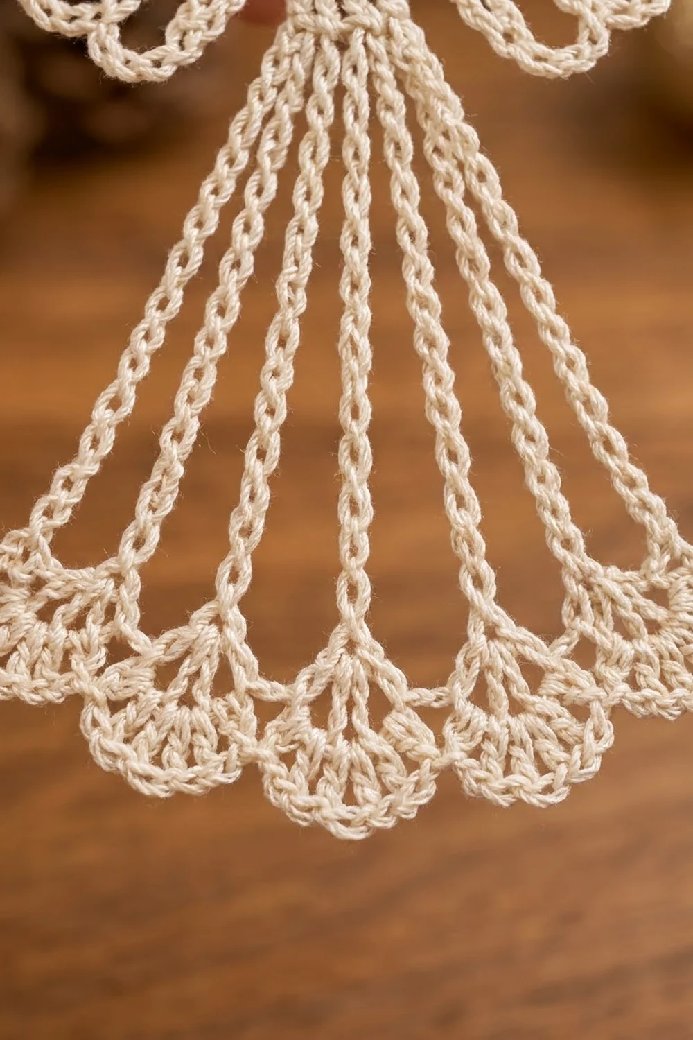 Close-up of cream-colored macramé with twisted rope strands and decorative scalloped knots against a warm brown backdrop.