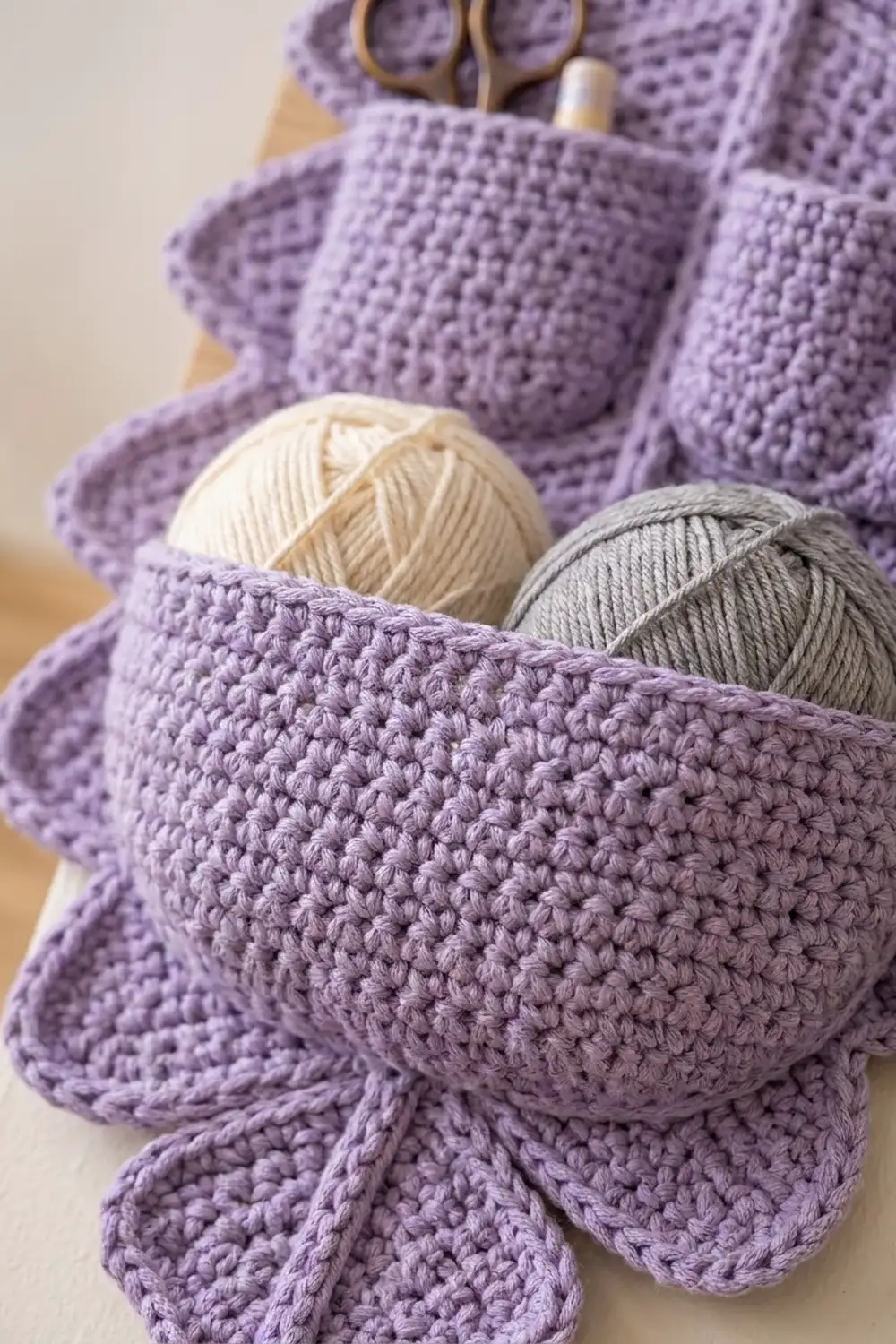 Lavender crocheted blankets with cream and gray yarn balls and bronze scissors on a neutral background.