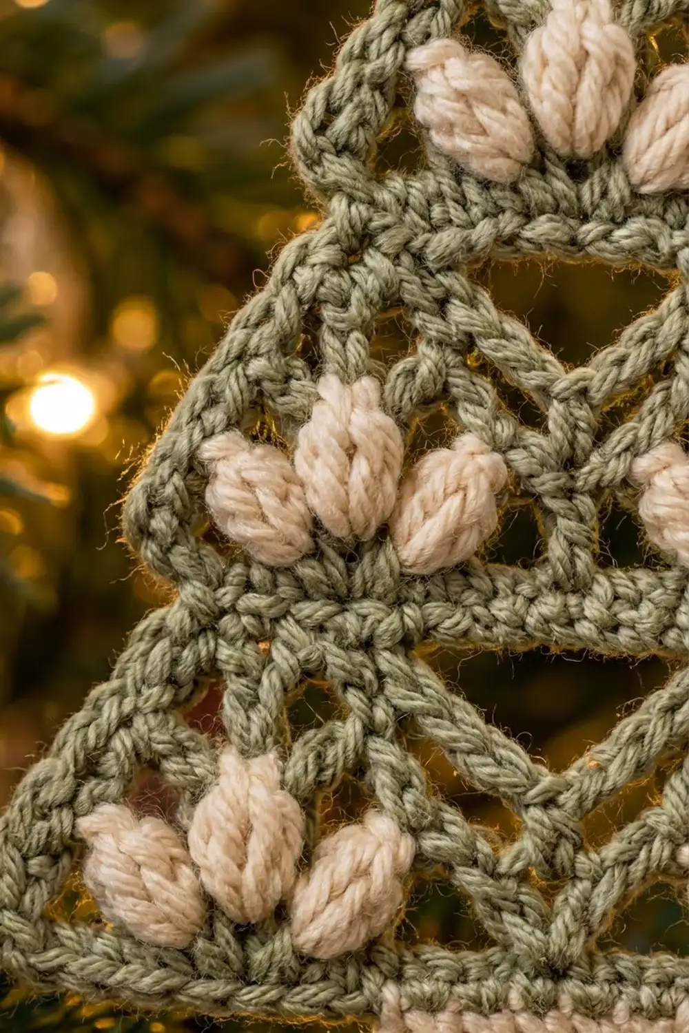 Sage green crocheted rope with cream popcorn bobbles creates textured lattice pattern against warm golden bokeh background.